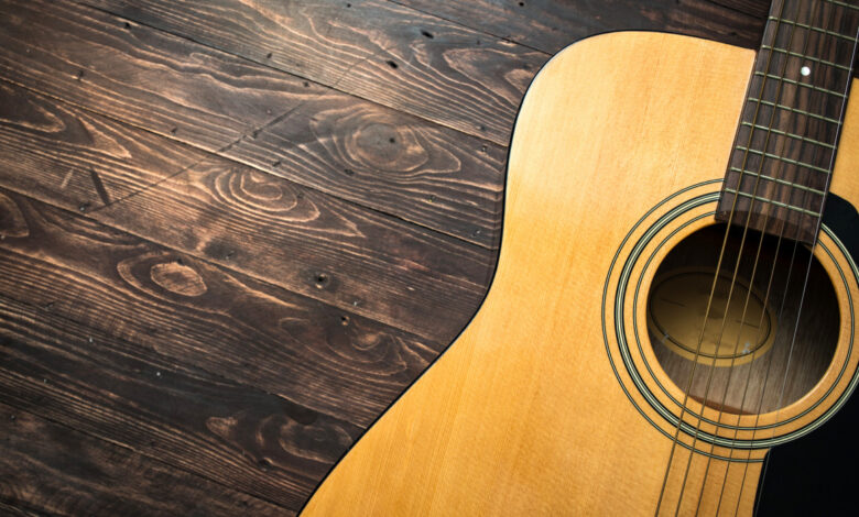 Acoustic guitar resting against a wooden background with copy space
