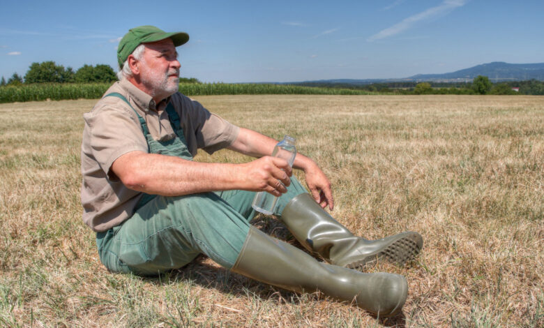 A farmer sits helplessly on his parched meadow with a bottle of water in his hand and looks thoughtfully at the sky. Climate change is causing his farmland to dry out more every year.