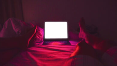 Adult couple watching series online in streaming platform bringin cinema at home, picture taken from personal perspective with legs and bright screen illuminating the bedroom with red light.