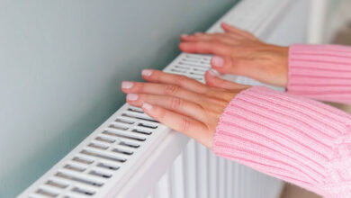 Close-up of a woman hands in a pink jumper keeping warm by a heating radiator. Energy crisis and cold weather concept