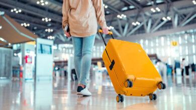 Young female traveler passenger walking with a yellow suitcase at the modern Airport Terminal, Back view of woman on her way to flight boarding gate, Ready for travel or vacation journey