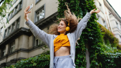 Portrait of young woman with smartphone dancing outdoors on street, tik tok concept.