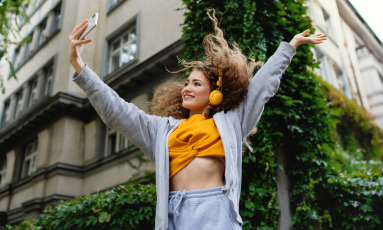 Portrait of young woman with smartphone dancing outdoors on street, tik tok concept.