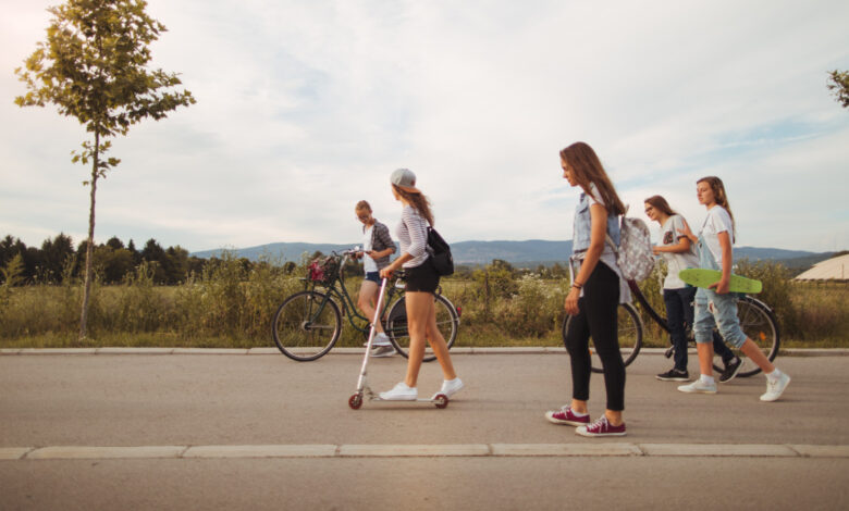 Photo of a teenage girls spending free afternoon together, riding bicycles, push scooters and skateboards