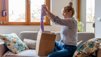 Happy young attractive woman open cardboard box satisfied with purchase online shop order sit on sofa at home.