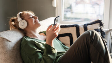 Young woman relaxing on a sofa and listening music on her phone via headphones