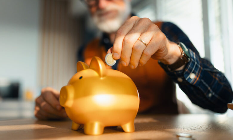 Senior man putting coins, money into a piggy bank. Saving Money after retirement, preparing for retirement. Financial education and financial literacy for seniors.