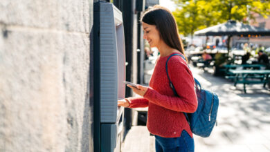 Young woman withdrawing money using phone at the ATM machine on the street in Copenhagen in Denmark.